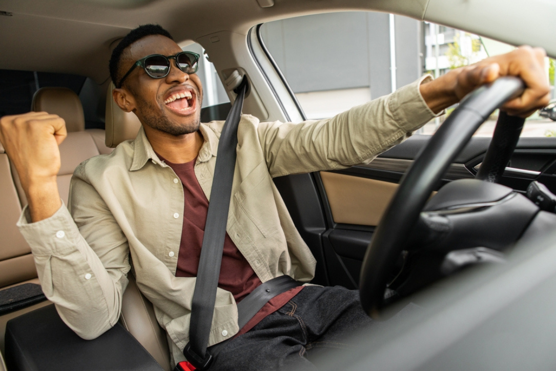 Joyful black man with glasses dances in car and sings while driving his car. fun street