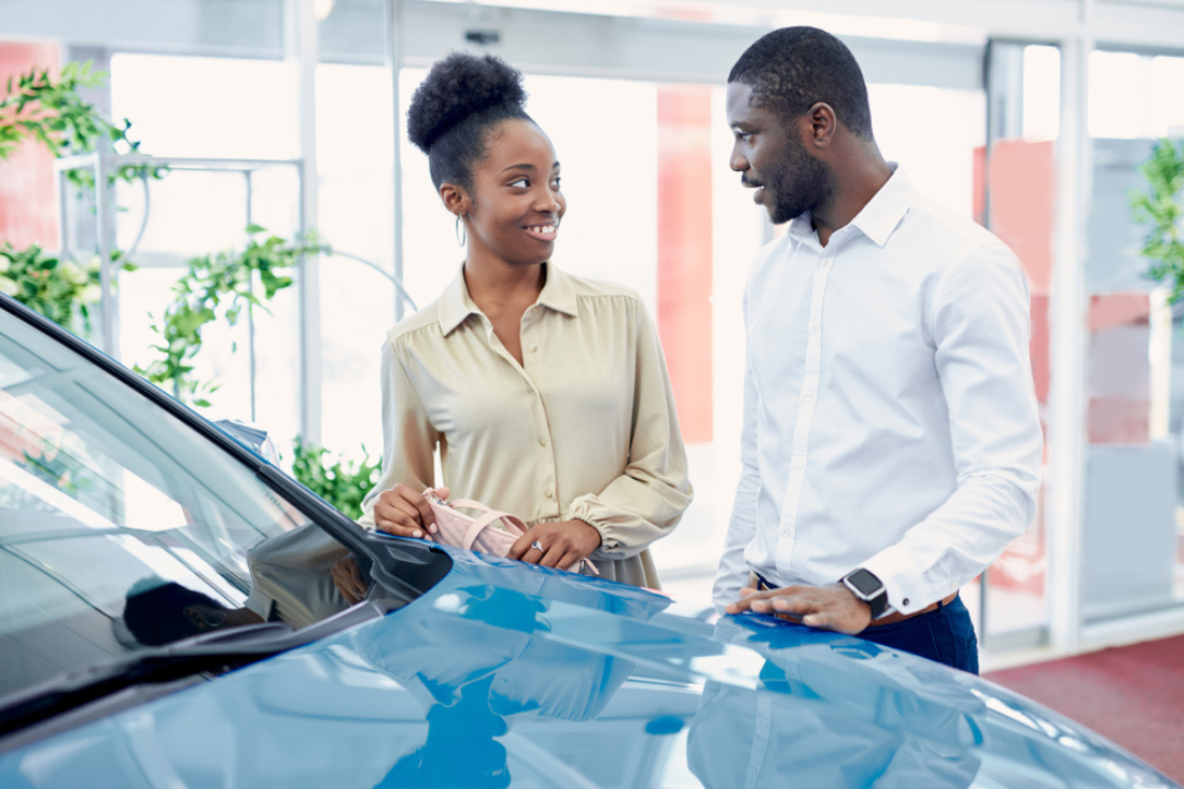 Young African married couple looking for the best car in the dealership, they are talking and discussing about cars.